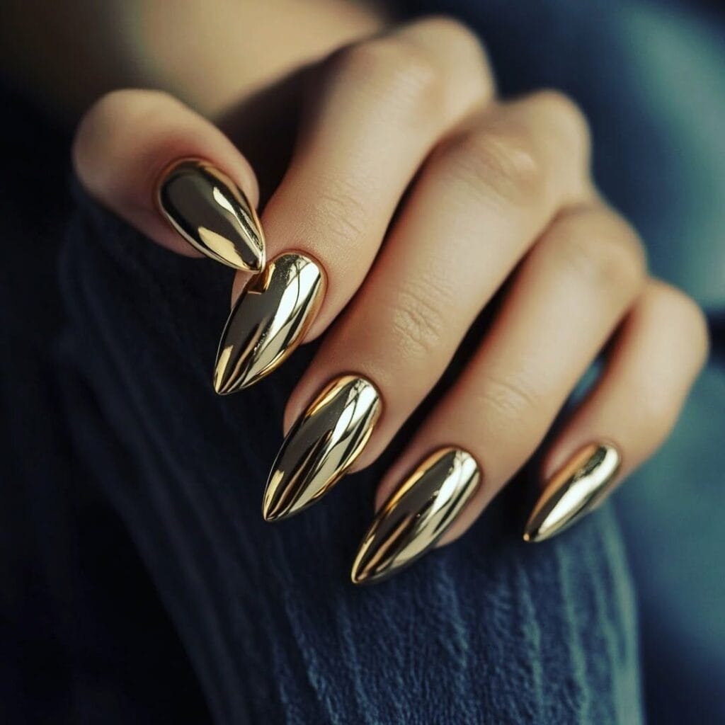 hand with long stiletto mirror-finish gold chrome nails resting on jeans.
