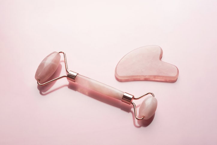 Close-up quartz roller and gua sha massage scraper on pink background. Facial massage tools. Skin care, beauty and health concept.