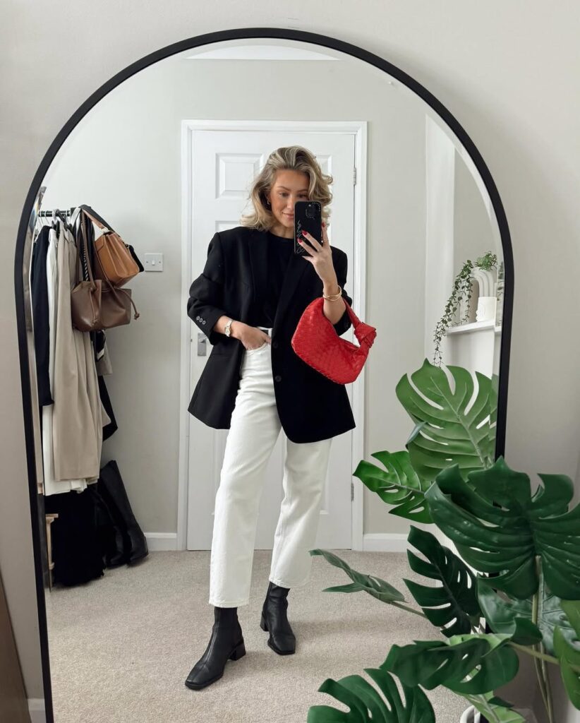 blonde woman wearing a black blazer and white jeans holding a red woven handbag
