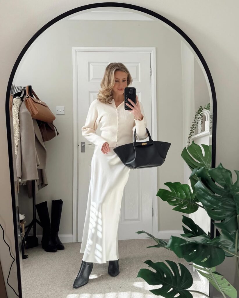 woman in a cream cardigan and white silk maxi skirt holding a large black handbag for spring outfits inspo