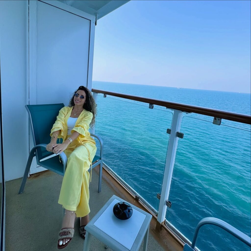 woman in a yellow two piece outfit sitting on a cruise ship balcony overlooking the sea