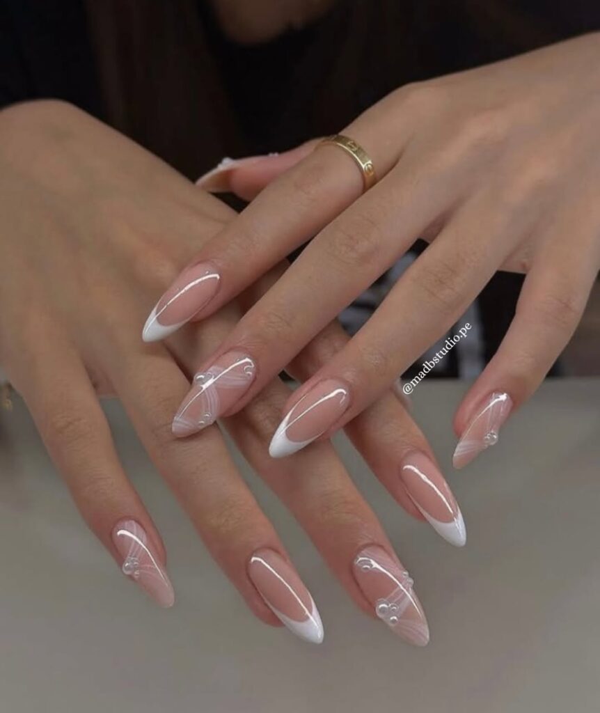 Hands with long, almond-shaped nails featuring a white French tip design and delicate embellishments.