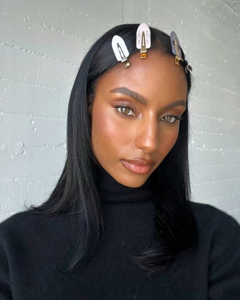 A woman with straight black hair adorned with decorative hair clips, wearing a black turtleneck sweater, and displaying a natural makeup look.