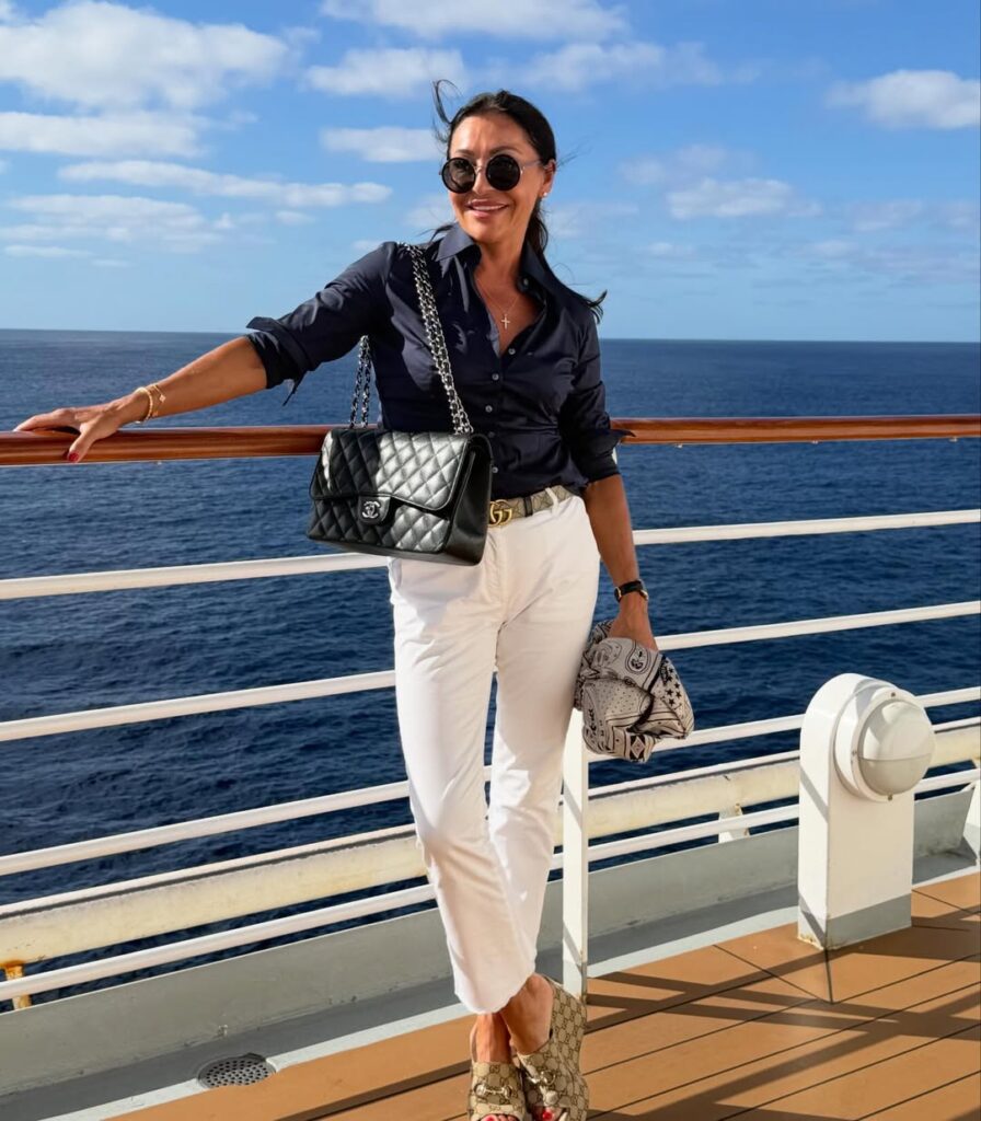 smiling woman in navy shirt and white pants stands on a cruise ship deck