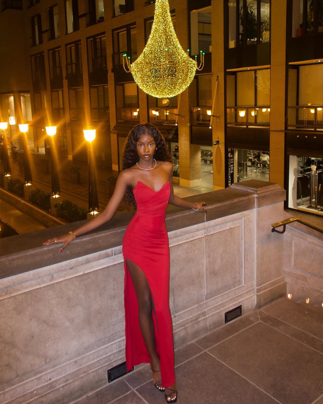 woman in a red strapless maxi dress with a thigh high slit posing on stairs.