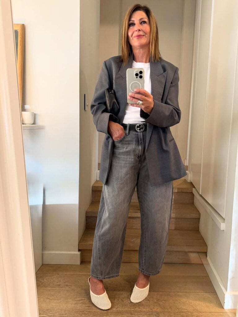 woman in oversized grey blazer and wide leg jeans taking mirror selfie on stairs