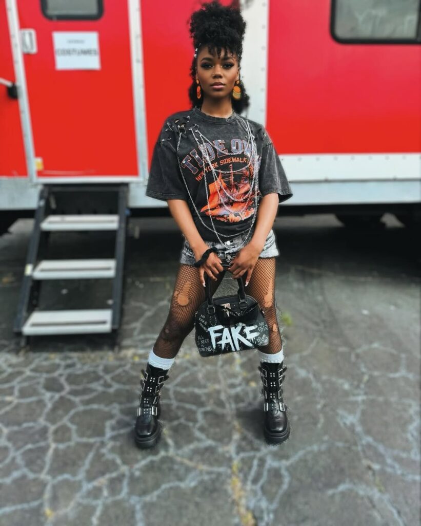 woman in punk rock fashion wearing a graphic t-shirt with chains, fishnets, and buckled boots