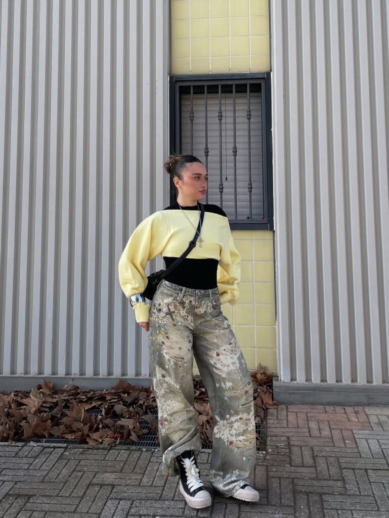 woman in y2k fashion wearing a yellow cropped sweater and distressed patterned baggy jeans