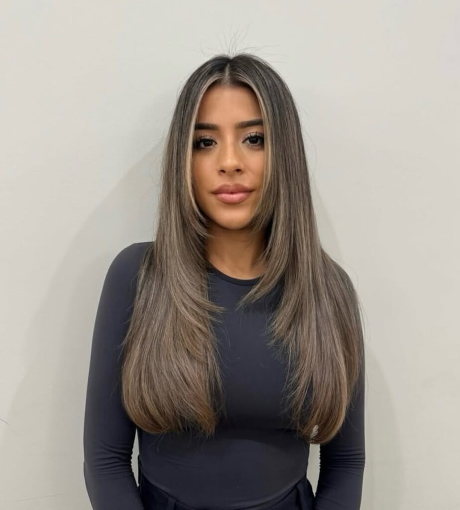 Woman with long, straight hair styled in a sleek manner, wearing a black long-sleeve top, posing against a neutral background.