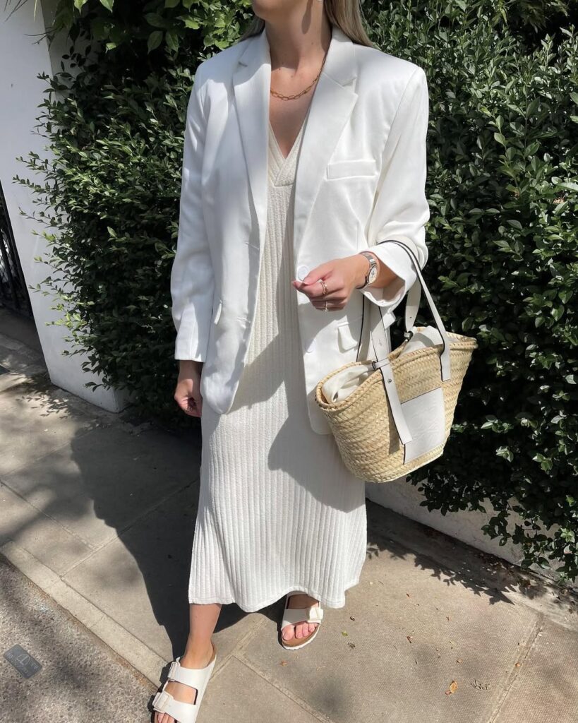 woman in white oversized blazer and ribbed maxi dress carrying a straw tote bag