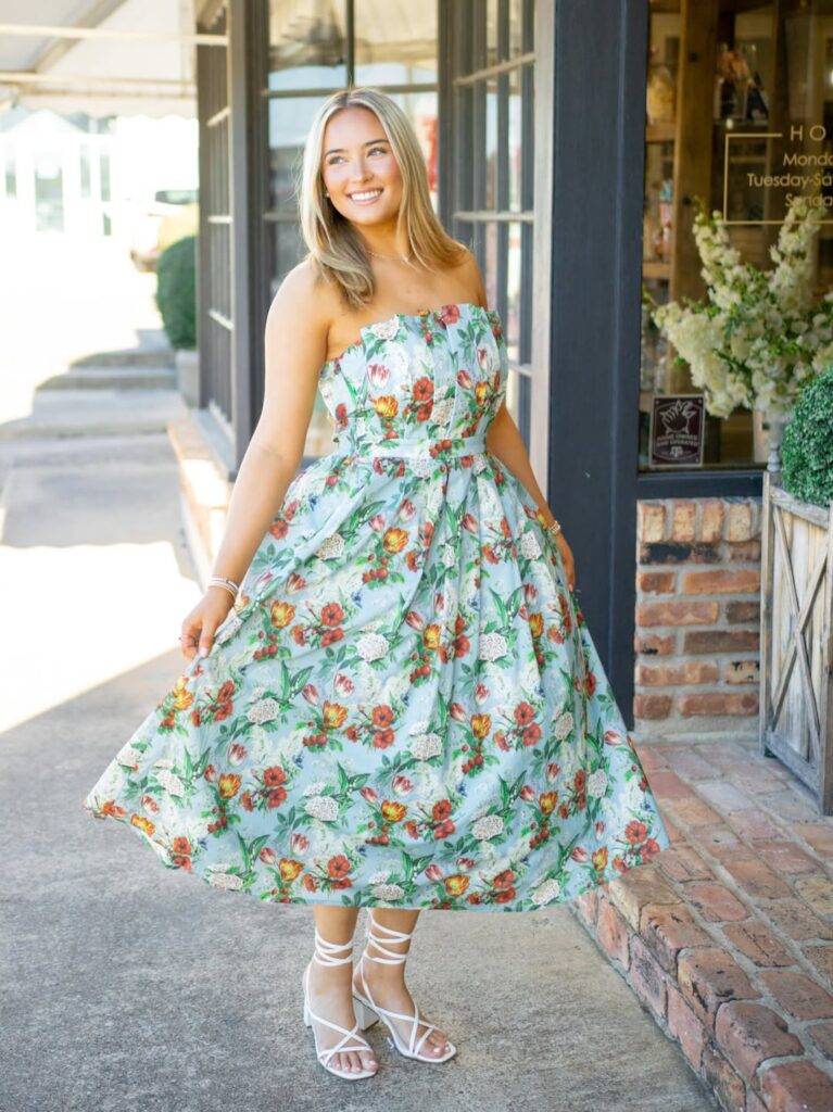 smiling woman wearing a light blue strapless floral midi dress and white lace-up sandals outdoors