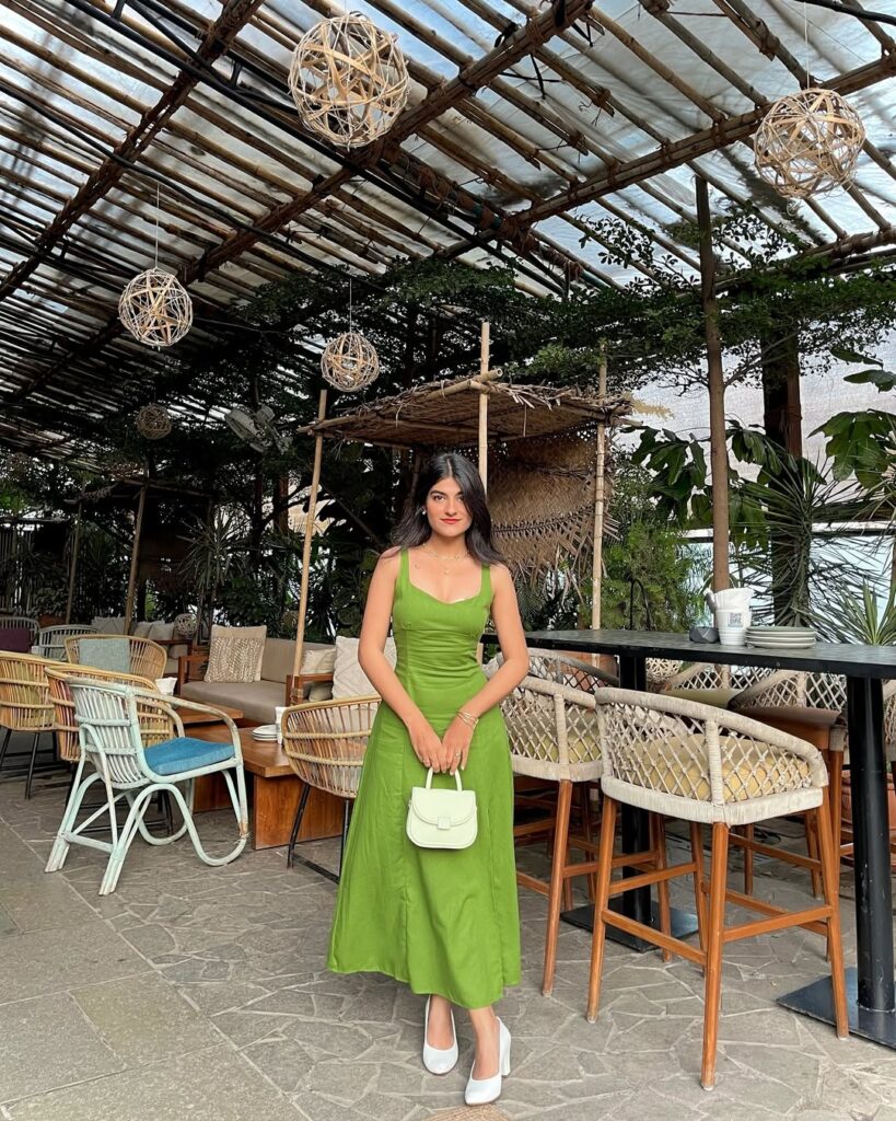 woman in green sleeveless midi dress and white heels holding small white handbag in cafe