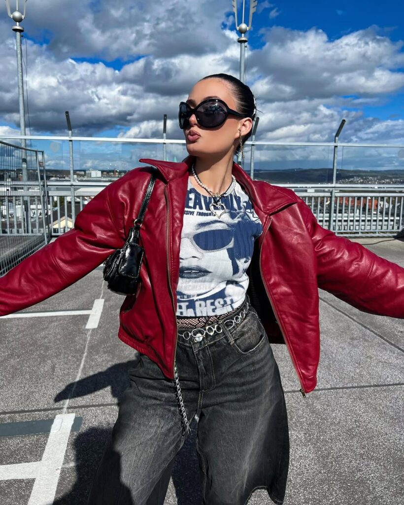 woman in y2k fashion wearing a red leather jacket, graphic tee, and baggy black jorts