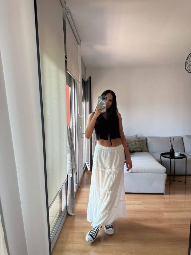 woman in black tie front crop top and white tiered maxi skirt taking mirror selfie