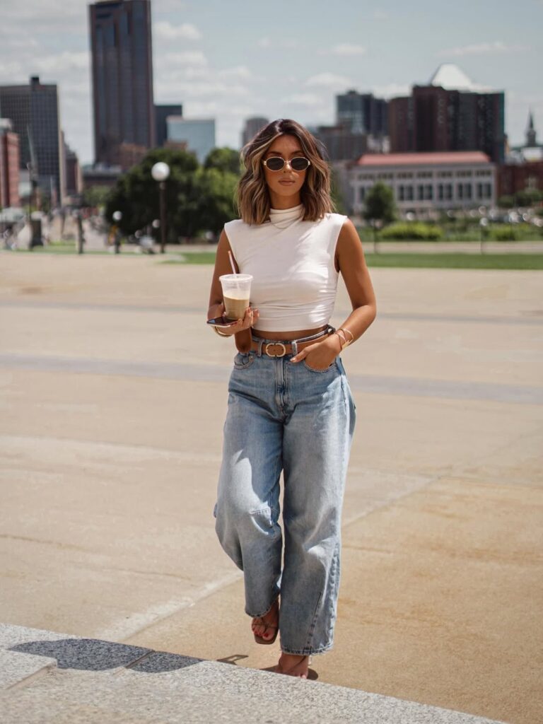 woman in a white sleeveless turtleneck and wide-leg jeans walking through a city plaza