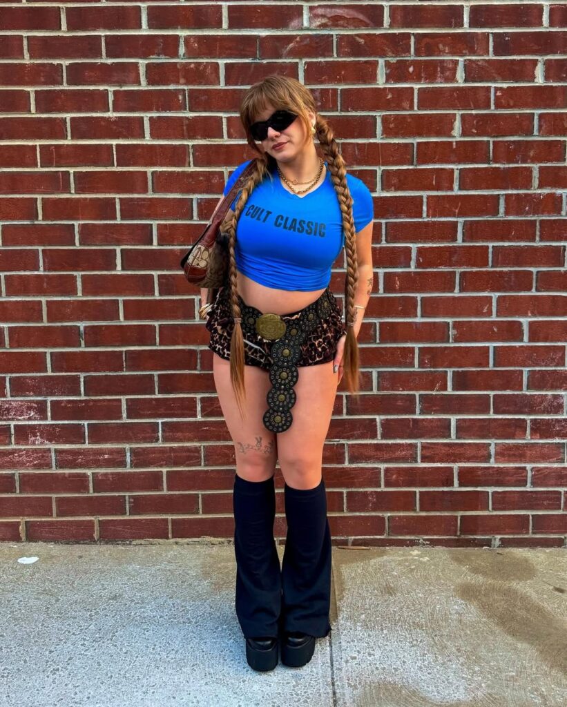 woman in y2k fashion wearing a blue graphic tee, leopard print skirt, and leg warmers