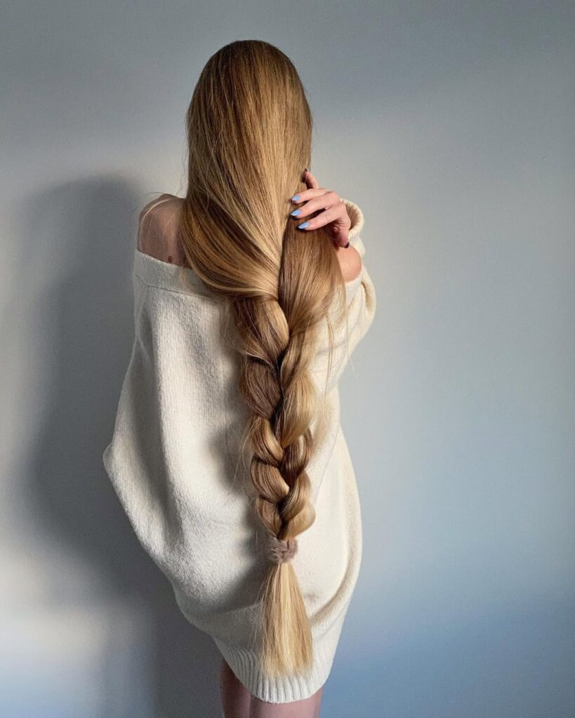 Long, braided hair cascading down the back of a person wearing a cream-colored oversized sweater.