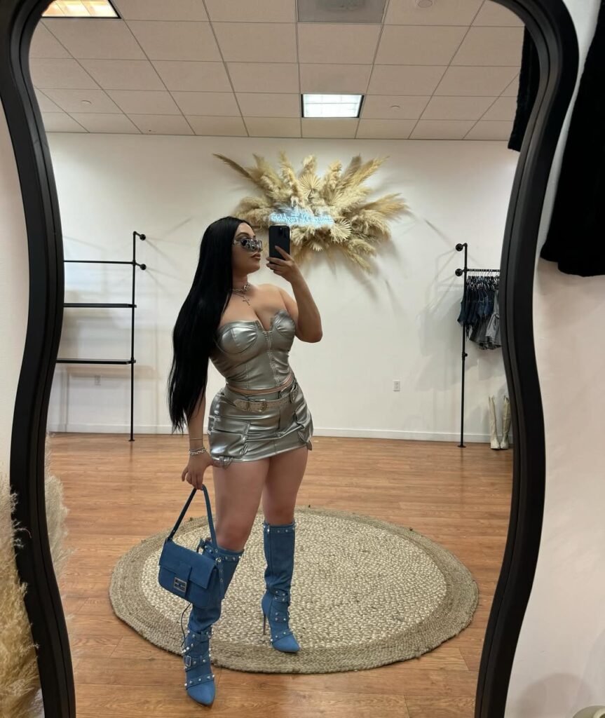 woman in metallic silver corset and mini skirt posing with blue denim boots in boutique mirror