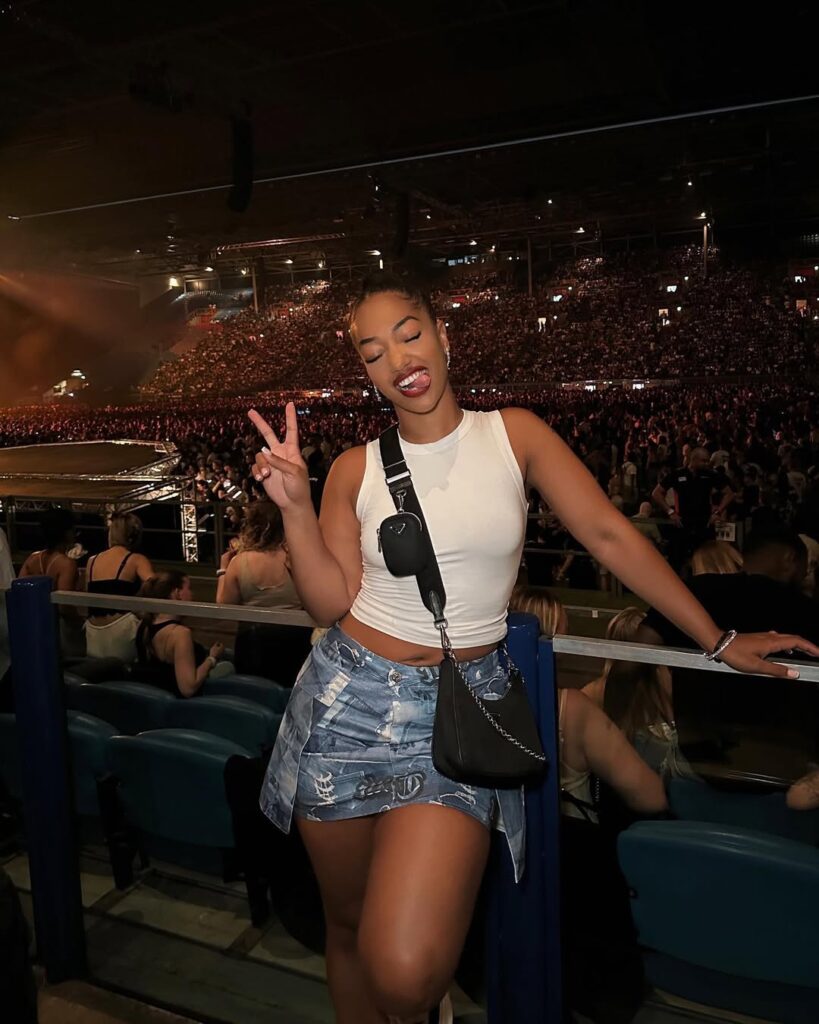 woman in white tank top and denim skirt posing at a crowded music concert venue