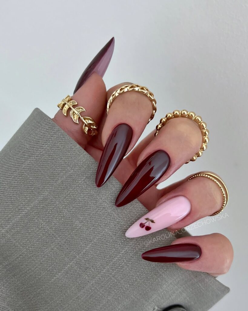 long almond cherry coke nails with gold rings and a light pink accent nail.