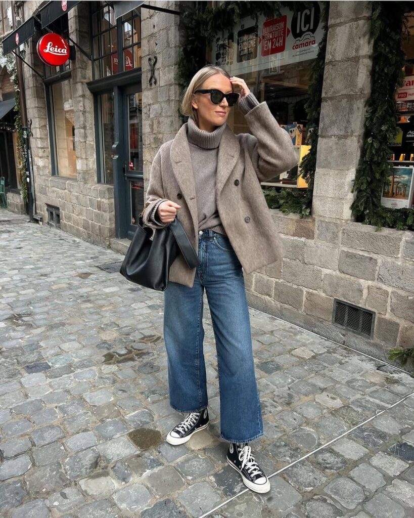 woman in brown wool jacket and wide leg jeans walking on cobblestone street