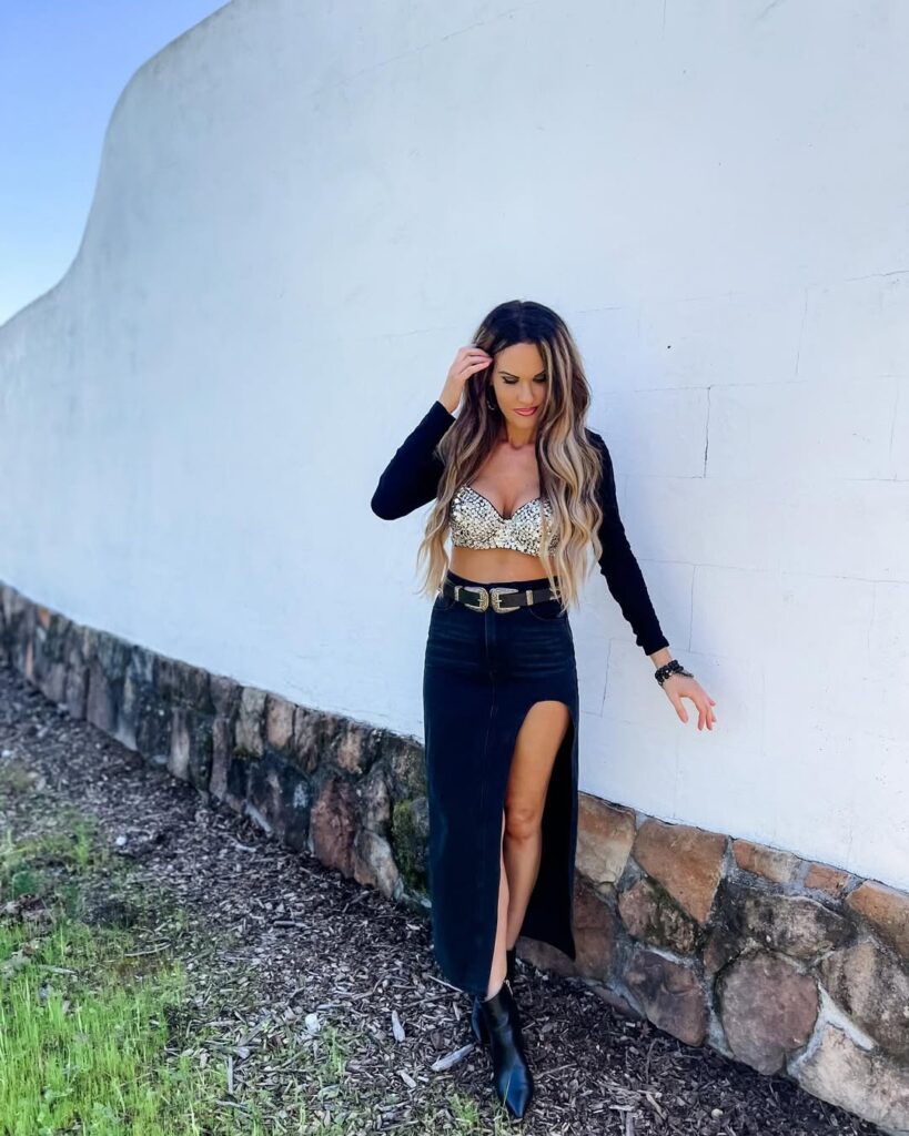 woman in sequin bra top and black maxi skirt with high slit posing against white wall