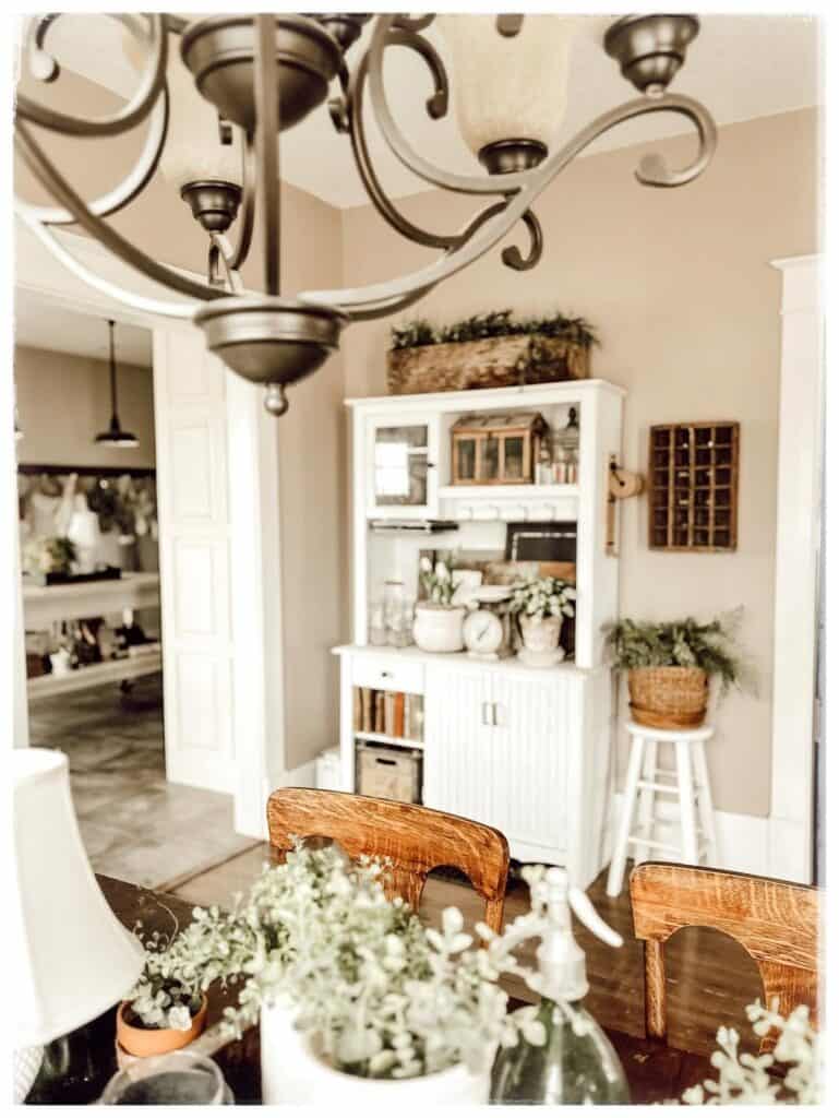 white farmhouse hutch decorated with potted plants and vintage kitchenware in a neutral room.