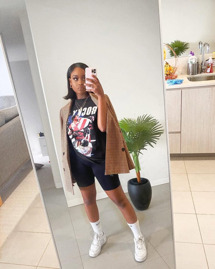 woman taking mirror selfie wearing rocky t-shirt with brown checkered blazer and bike shorts