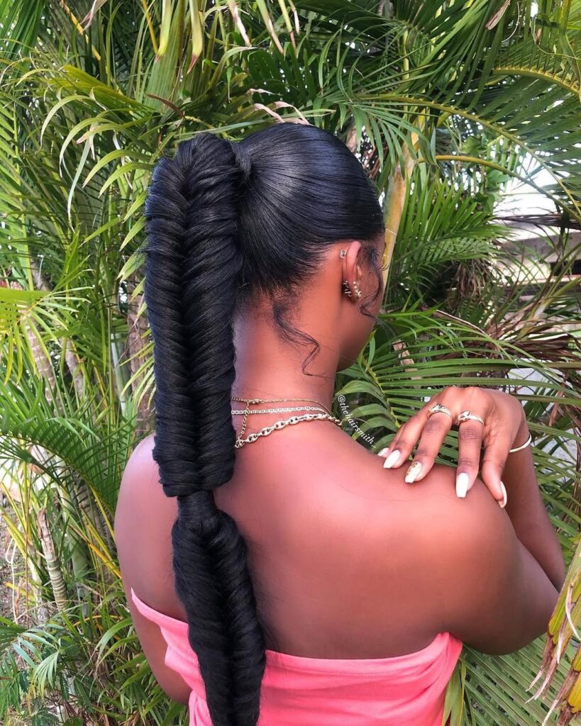 woman with a sleek fishtail braid ponytail posing against tropical palm tree leaves