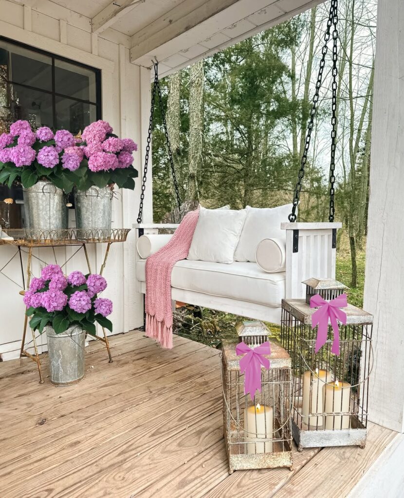 white porch swing with a pink throw blanket next to purple hydrangeas and lanterns.