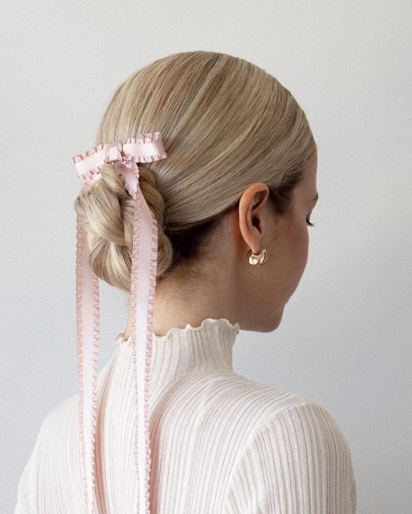 blonde woman with hair styled in a low braided bun with a long pink ribbon