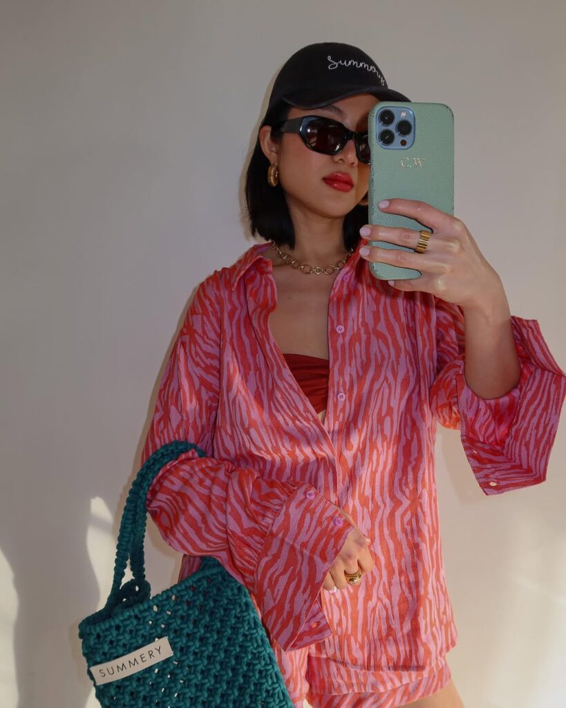 woman in pink and orange patterned shirt holding a green woven summery copenhagen bag