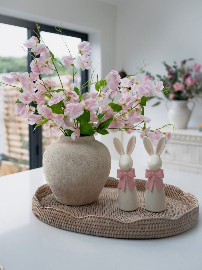 pink sweet pea flowers in a stone vase next to white ceramic bunny figurines.