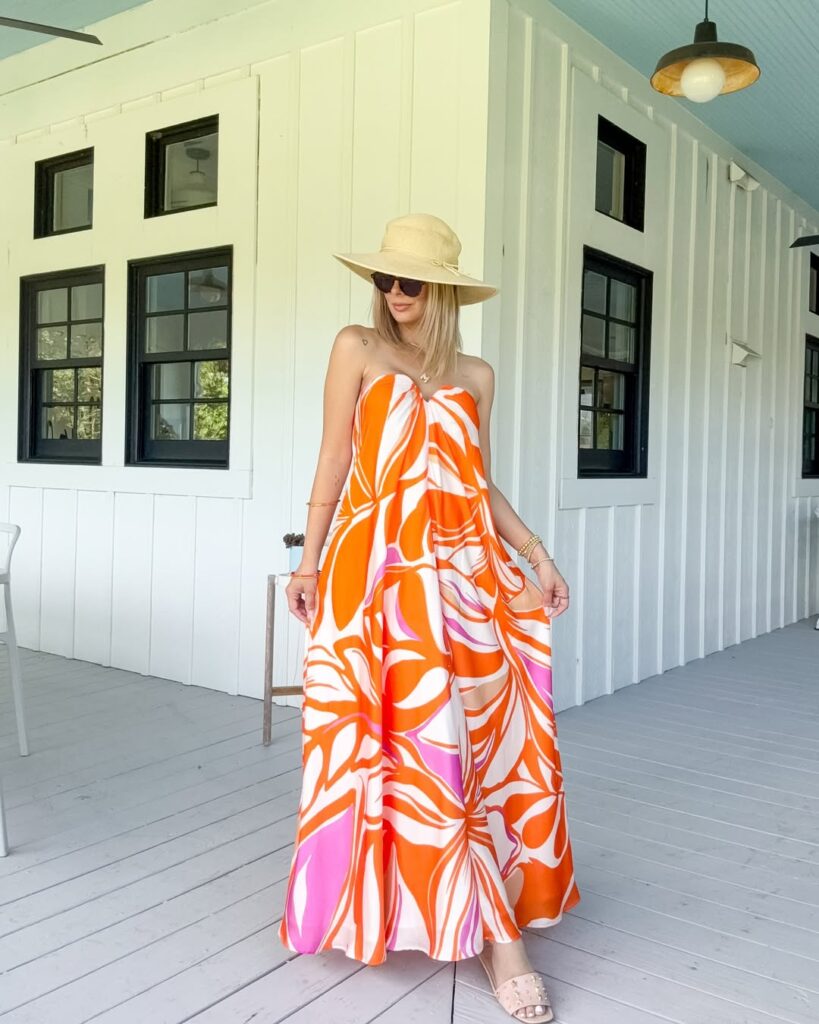 blonde woman wearing a straw hat and orange floral maxi dress on a white porch