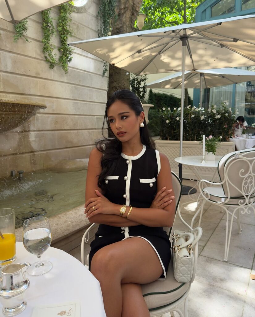 woman in black sleeveless dress with white trim sitting at outdoor cafe table