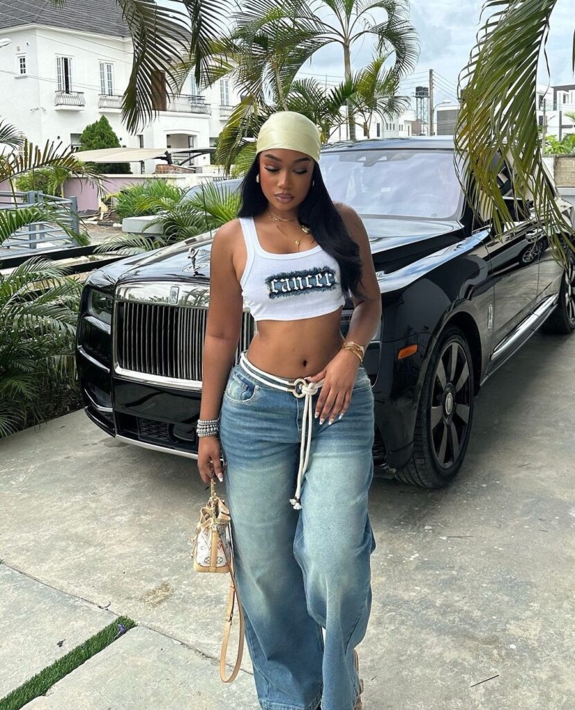 woman wearing a cancer graphic crop top and baggy jeans in front of a luxury car