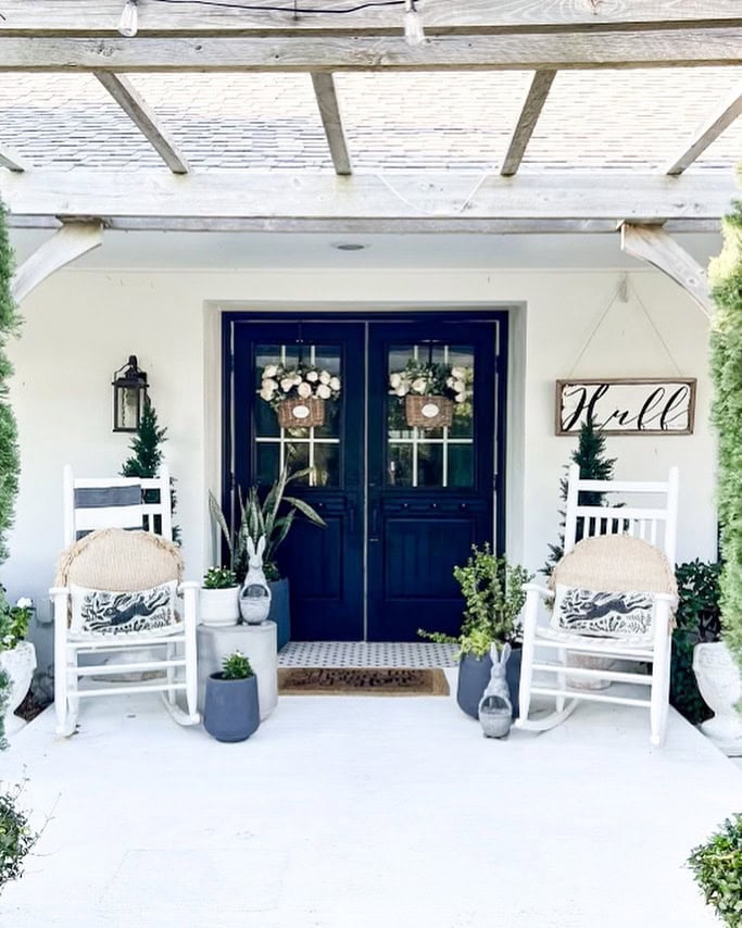 white porch with rocking chairs, navy double doors, and white rose baskets in the windows.
