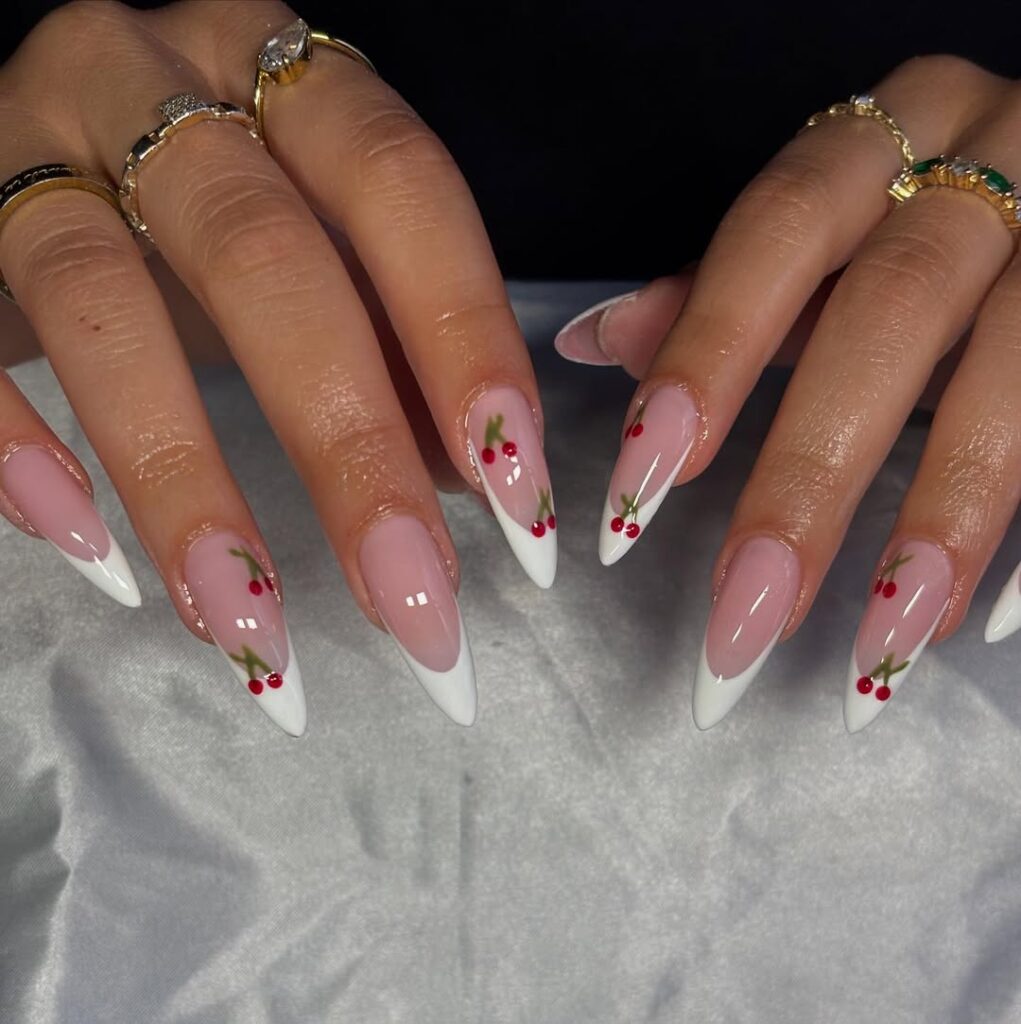 white french tip almond nails with small red cherry decals and gold rings