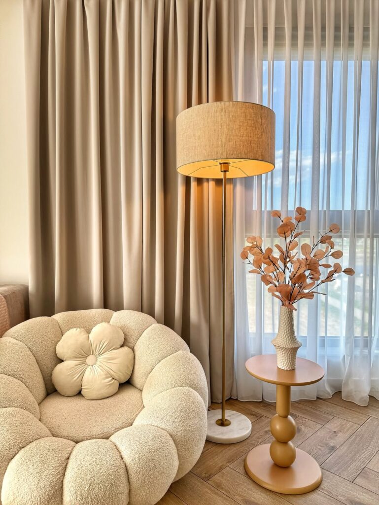 beige textured armchair with a flower shaped pillow beside a tall floor lamp.