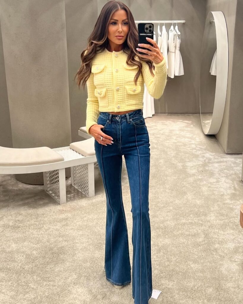 woman in yellow tweed cropped jacket and dark wash flare jeans taking a mirror selfie
