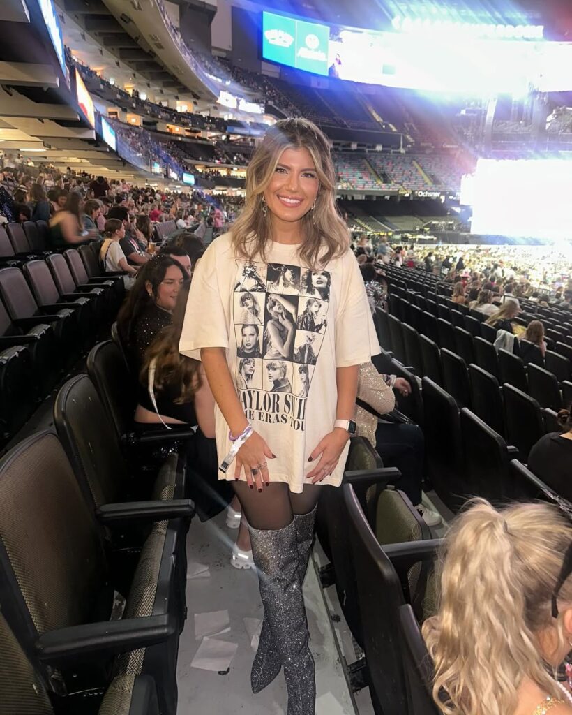 smiling woman wearing oversized taylor swift eras tour t-shirt and sparkly silver knee-high boots indoors