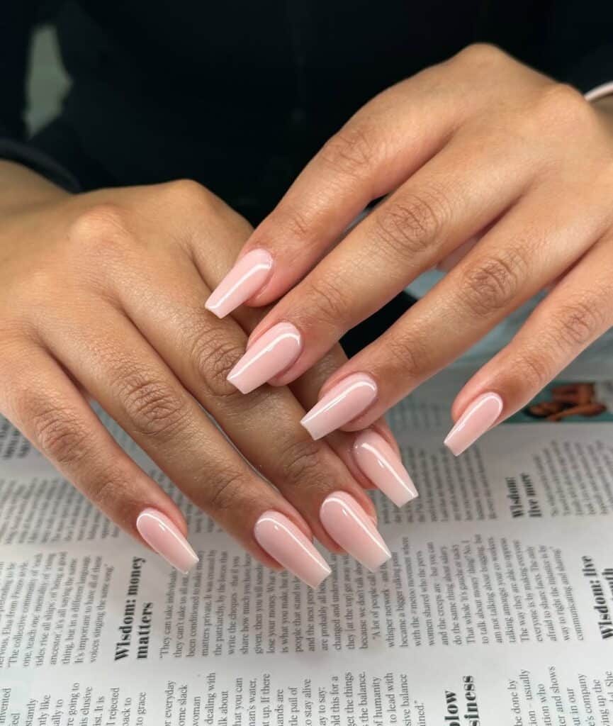 long square nude nails with a glossy finish on a newspaper background