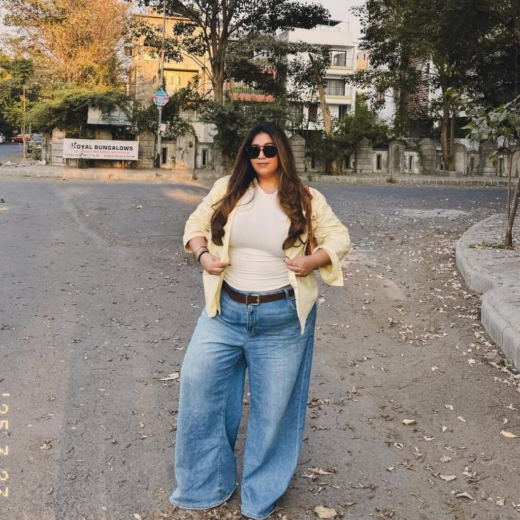 woman wearing light yellow shirt and wide leg jeans standing on paved road
