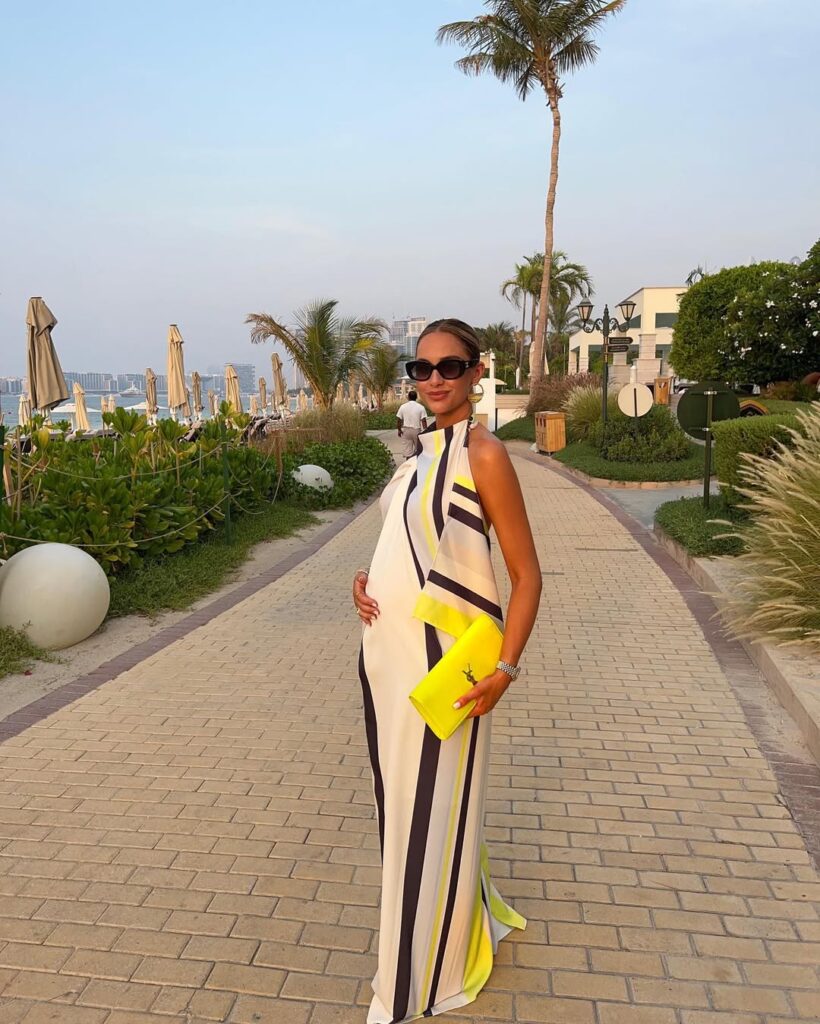 woman in striped maxi dress holding yellow clutch on beach walkway