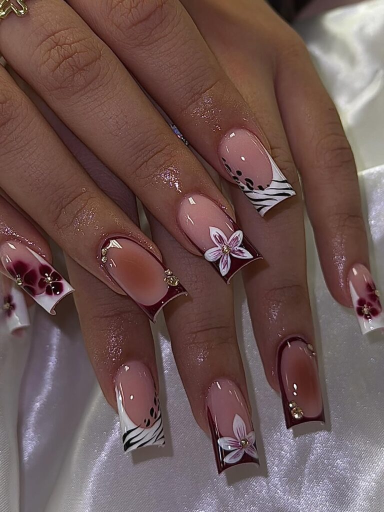 long square nails with zebra print tips, burgundy accents, and white 3d floral art