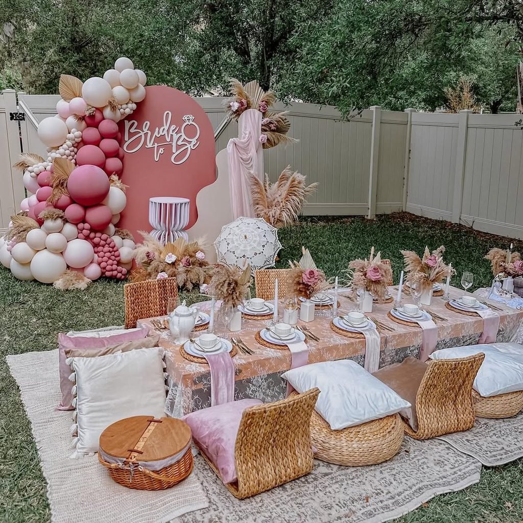 boho picnic bridal shower featuring low tables, floor cushions, and pink balloon arch backdrop