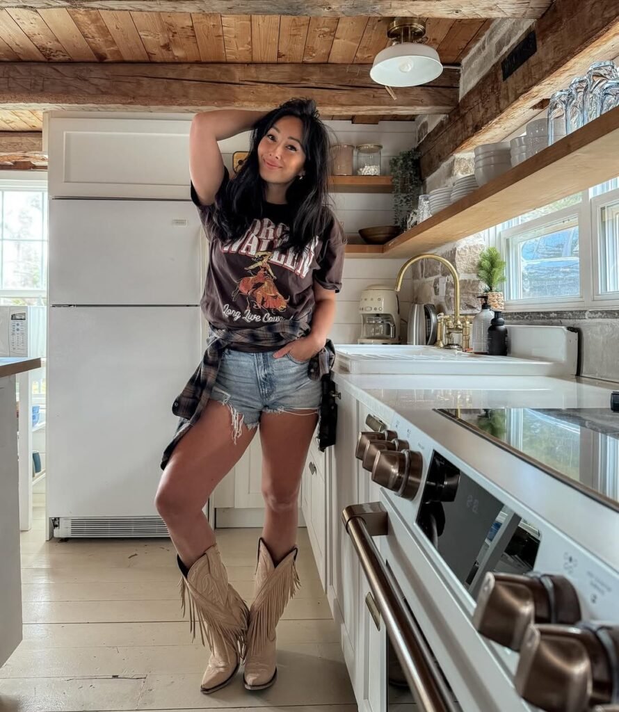 woman wearing graphic tee denim shorts and fringed cowboy boots in a rustic kitchen