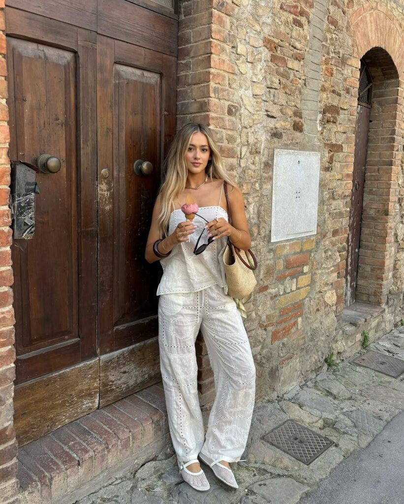 woman in white eyelet summer outfit holding gelato in front of a rustic door