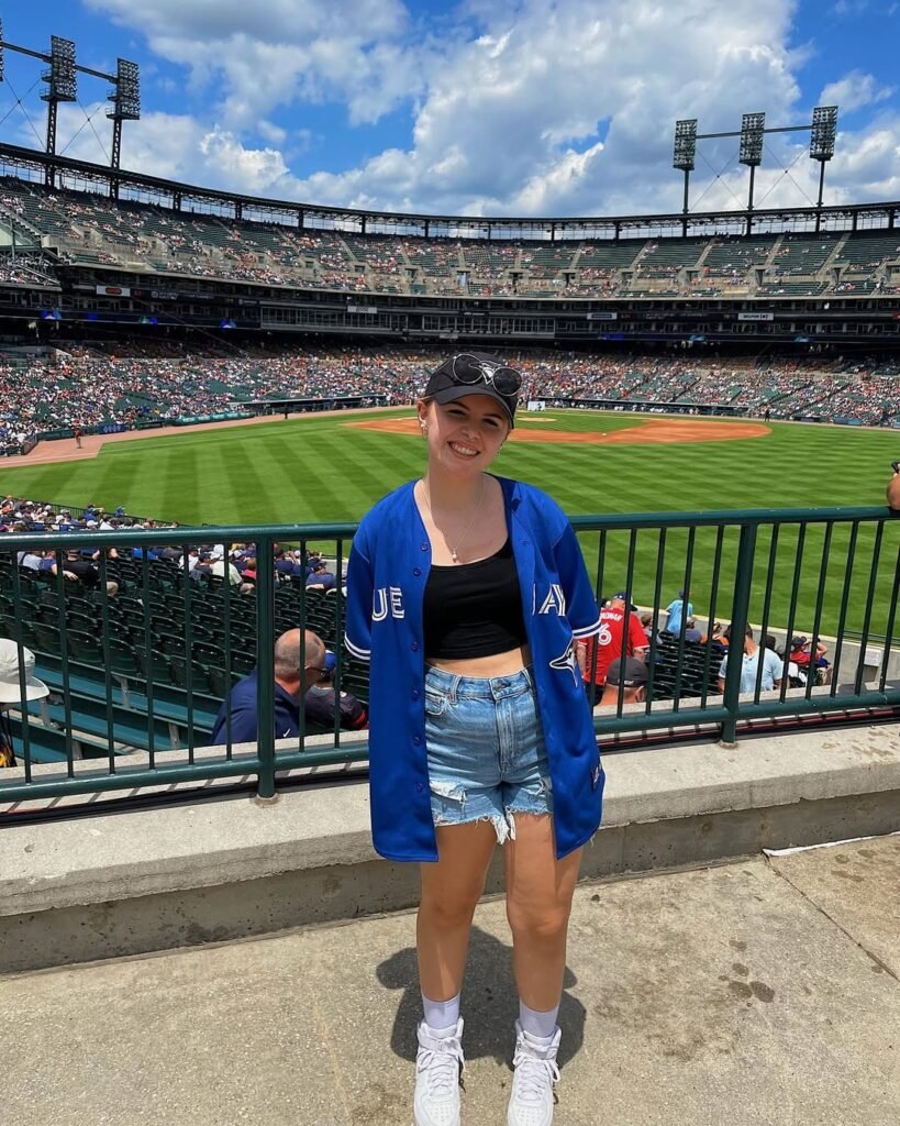 Woman in blue Blue Jays jersey and denim shorts smiling at baseball stadium