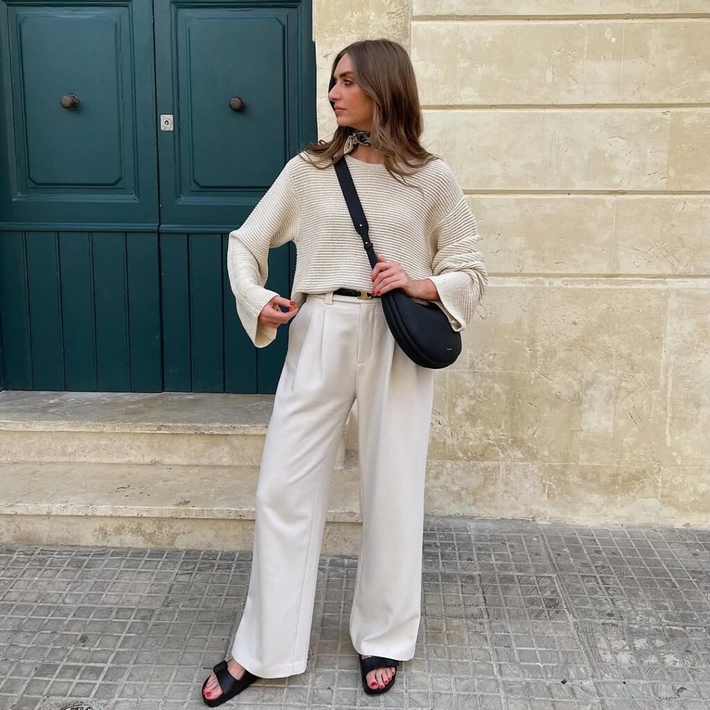woman in cream ribbed sweater and wide leg trousers standing by a green door